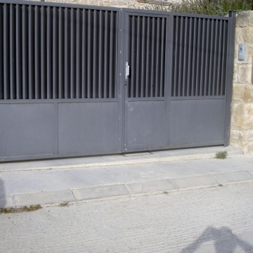 Porta batent de dues fulles, motoritzada, amb portella d’accés i pintada de negre forja